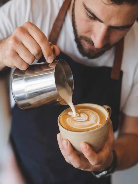 Barista gießt Latte-Art in eine Tasse
